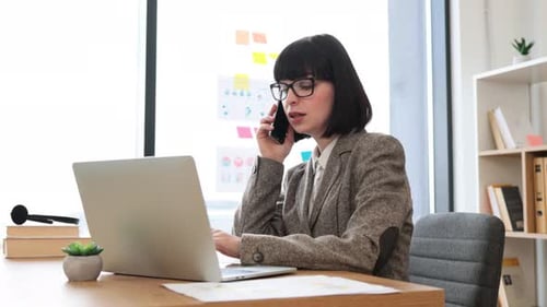 Woman Works and Talks on Phone at Desk