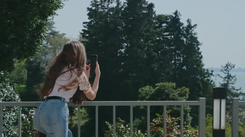 Relaxed Woman Takes Smartphone Photo Standing on Hill Overlooking Sea