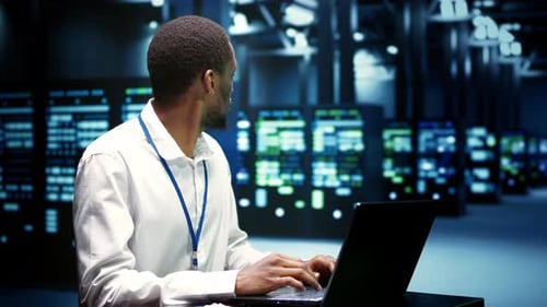 Man Works on Laptop in Data Center