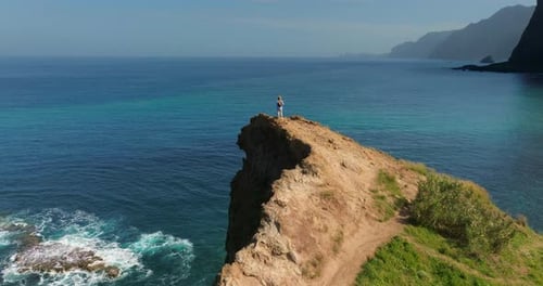 Woman in Hat Enjoying of Ocean Woman Standing Up High on a Cliff Edge Rear View Happy Traveler