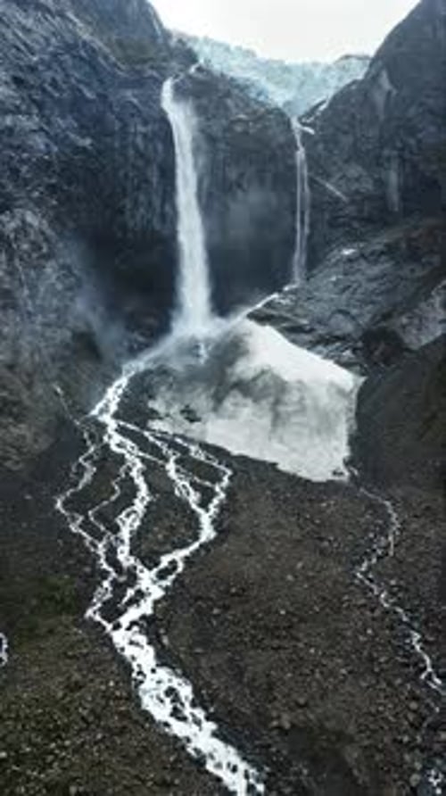 Aerial drone view of the powerful twin streams of a glacier fed waterfall surrounded by rocky cliffs