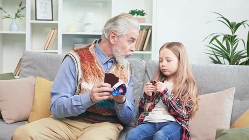 Senior Man and Child Eating Chocolate on Sofa