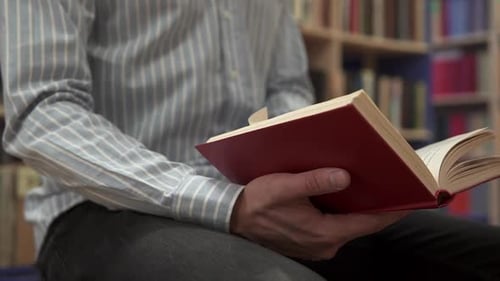 Ein Student sitzt zwischen Bücherregalreihen und liest ein Buch, um sich auf eine Prüfung vorzubereiten.