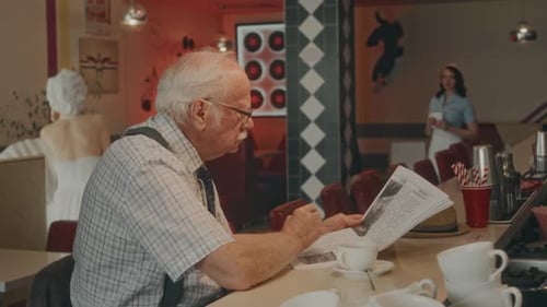 Senior Gentleman Reading Article in Morning Newspaper in Retro Diner