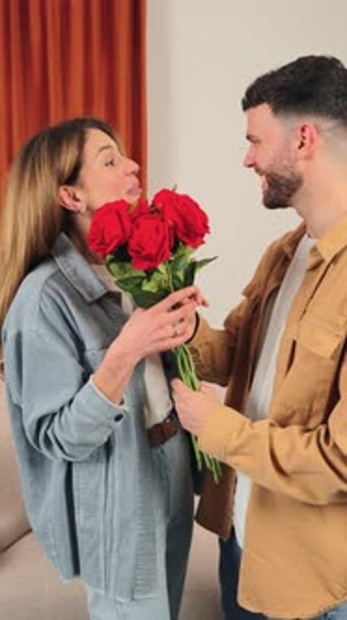 Smiling Young Couple with Red Roses Embrace Indoors