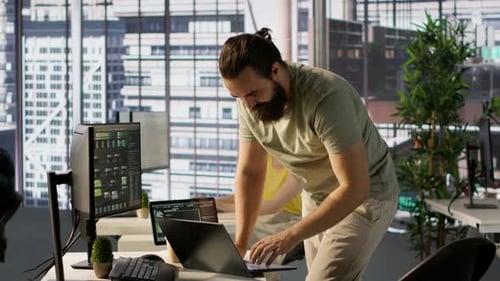 Mann überwacht Firmensysteme mit einem Notebook, während er im Büro steht