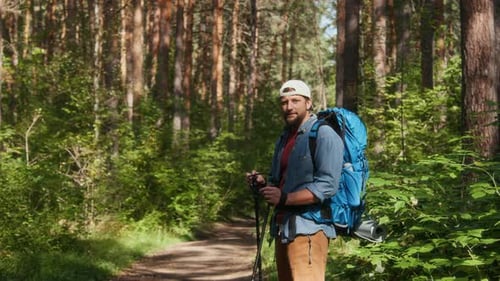 Male Hiker Standing on Path in Dense Forest with Backpack and Trekking Poles