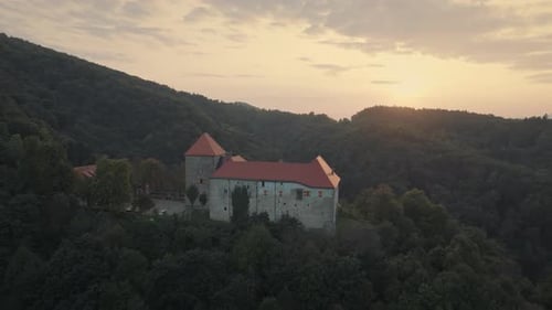 Luftaufnahme der mittelalterlichen Burg auf dem Hügel bei goldenem Sonnenuntergang. Das Schloss ist von tiefem Grün umgeben