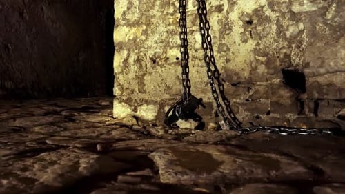 Iron chains hanged on stone walls of dungeon inside medieval castle, fear and terror scenery