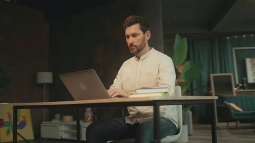 Handsome Man Sitting at Desk Use Laptop and Phone in the Office Look Serious Businessman Camera