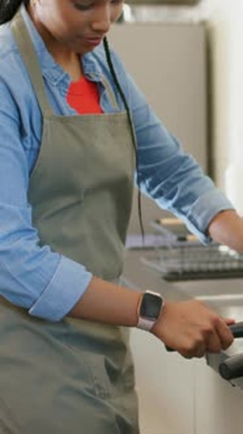 Vertical video: Reaching for metal lever, woman in olive-green apron pulling shot at counter