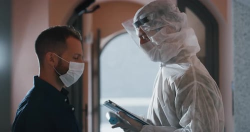 A man is getting temperature measured with infrared thermometer gun by medical staff with PPE suit