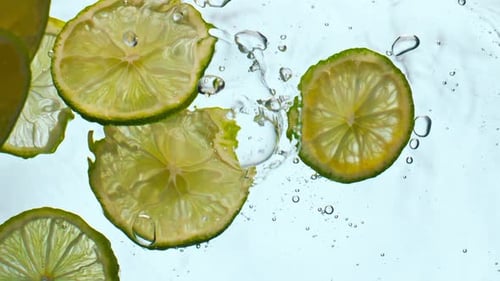 Fresh lime slices falling into clear water in super slow motion close up