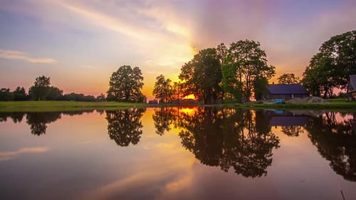 A golden sunset reflecting off a lake with a cabin on the shore - time lapse