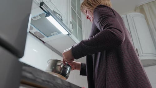 Joyful Lady Dancing While Cooking in Plaid Clothing Holding Pot in Kitchen