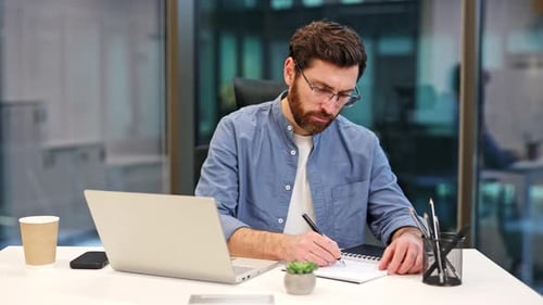 Businessman Writing in Notebook at Office Desk