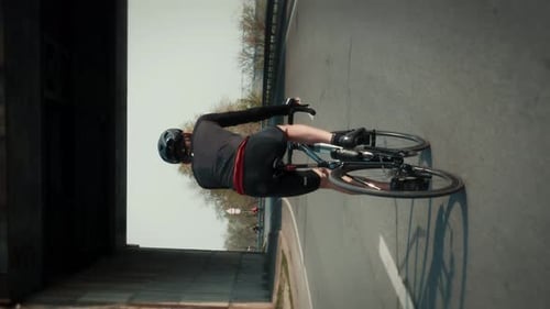 Man in black cycling apparel riding bicycle on cycle path in park.Vertical video