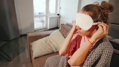 A Young Woman at Home Wrapped in a Cozy Blanket Puts on a Sleep Mask and Falls on Her Pillow Ready
