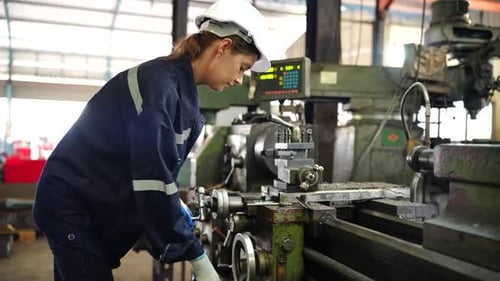 Eine Fabrikarbeiterin richtet in der Werkstatt eine CNC-Drehmaschine ein.
