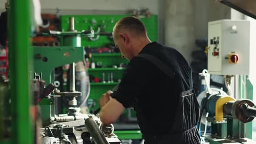 A mechanic in a workshop repairs a part with a hammer; various repair tools hang in the background