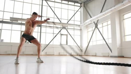 Shirtless Man Exercising with Battle Ropes in Gym