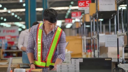 Asian warehouse worker pack the product package in counter of production line then use computer