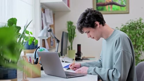 Young Male College Student Studying at Home Using Laptop Looking at Camera