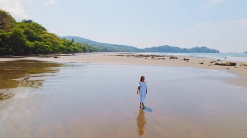 Woman in white dress walks on the reflective sand of Dominicalito beach in Costa Rica