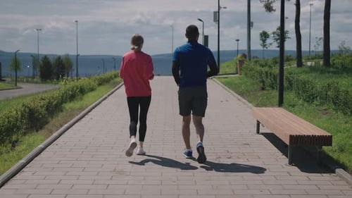 View From the Back A Man and a Woman Run Together in the Park on the Waterfront The Couple Goes in