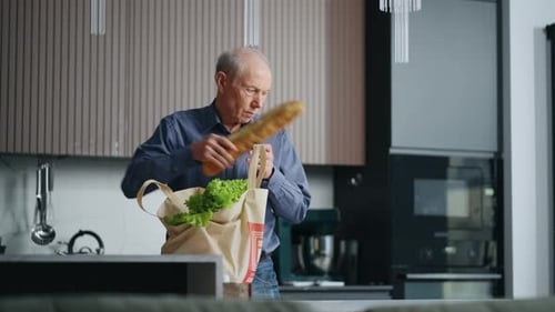 Anciano soltero desempacando las compras del supermercado poniendo una bolsa de tela ecológica con comida en la mesa de la cocina