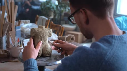 A Bearded Male Sculptor with Glasses Makes a Statue of a Female Figure A Ceramist Man Sculpts a