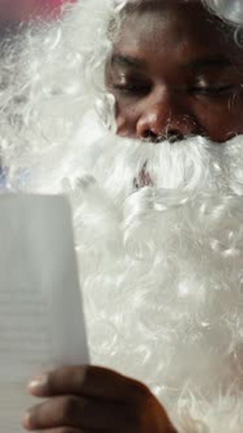 Vertical Video Black Santa Checking a Letter While Sitting in His Rustic Festive Cabin