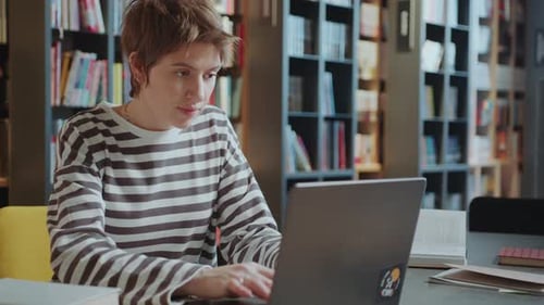Female Student Using Laptop and Writing Notes in Library