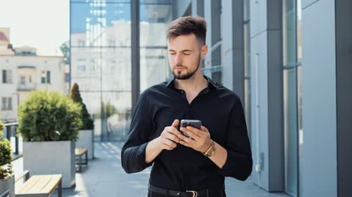 Attractive Man Typing Message in Mobile Thinking and Smiling