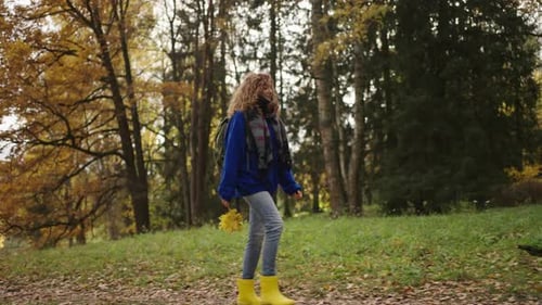 Woman in a Blue Sweater and Yellow Boots Walks in the Autumn Park and Enjoys the Beauty