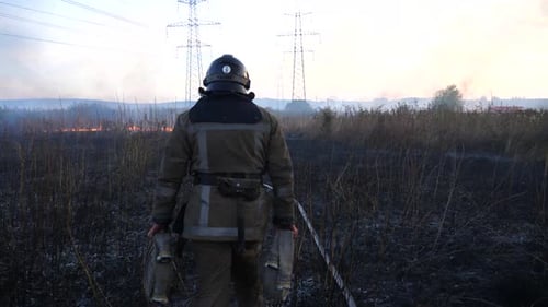 Firefighter Walking Toward Wildfire in Rural Field