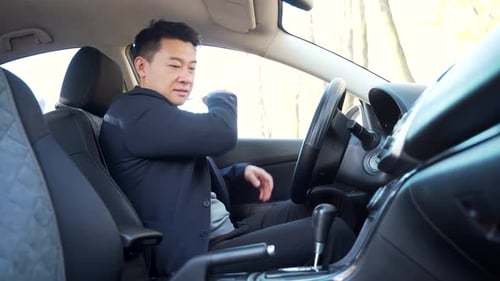 asian male driver fastens seat belt sitting in car. Protection of a person in vehicles. Compliance