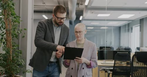 Man and Woman Coworkers Walking in Office Reading Document and Talking Discussing Project