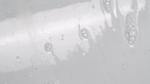 Seifenwasser fließt auf eine weiße glänzende Wand. - Nahaufnahme