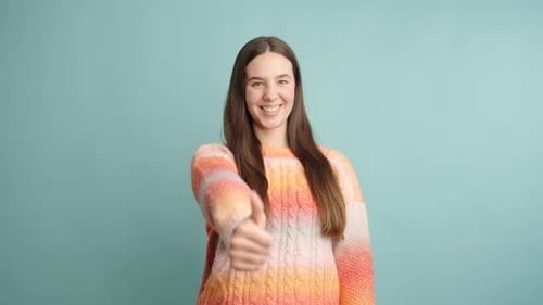 Mujer joven mostrando los pulgares para arriba y celebrando el éxito sobre fondo turquesa