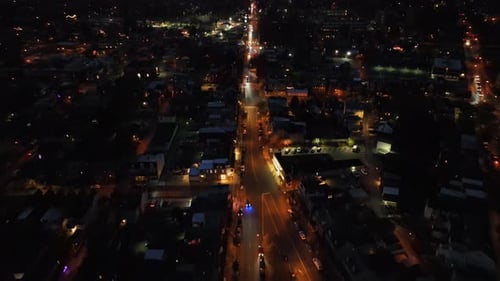 Aerial establishing shot of american town with warm lighting streetlights along road at night. Top d