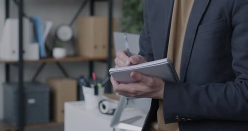 Closeup of Male Hand Writing in Notebook While Businessman Working in Office