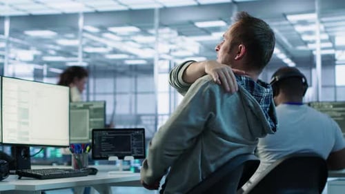 Man Stretches Before Typing at Computer in Office