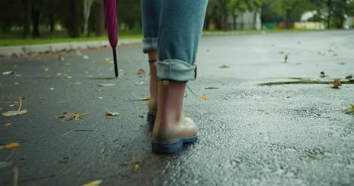 Close Up a Girl in Boots Walks Along the Asphalt and Falls in the Autumn Park After the Rain