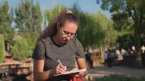 Young Woman Sits and Writes in Urban Park