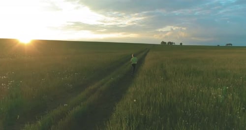 Sporty Child Runs Through a Green Wheat Field in Summer Rain