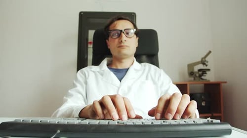Slow Motion a Man in a White Coat and Glasses Works Intently on a Computer Scientific Activity of a