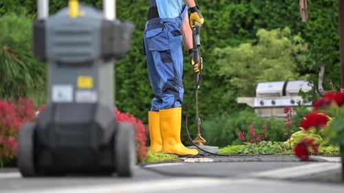 Man Using a Pressure Washer to Clean Pathways in a Garden During Summer
