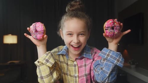 Portrait of a Caucasian Child in a Pink Shirt Holds Two Pink Glazed Donuts in His Hands Near His