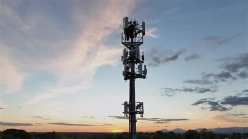 Aerial orbit shot of Telecommunication Tower in american town at golden sunset. Forest landscape in